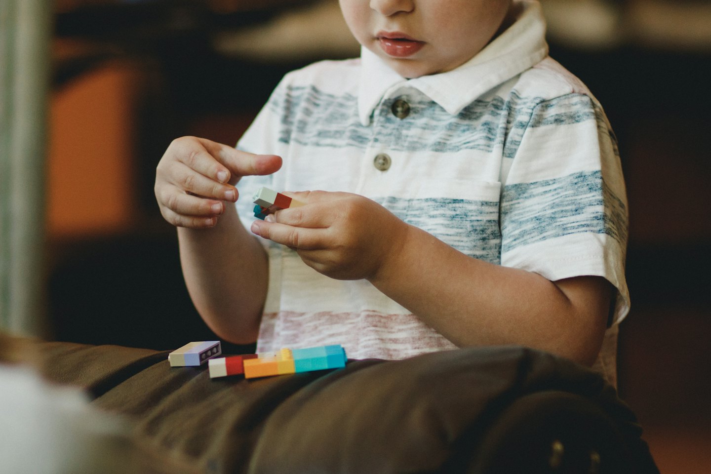 Child plays with colorful building blocks on a brown cushion.