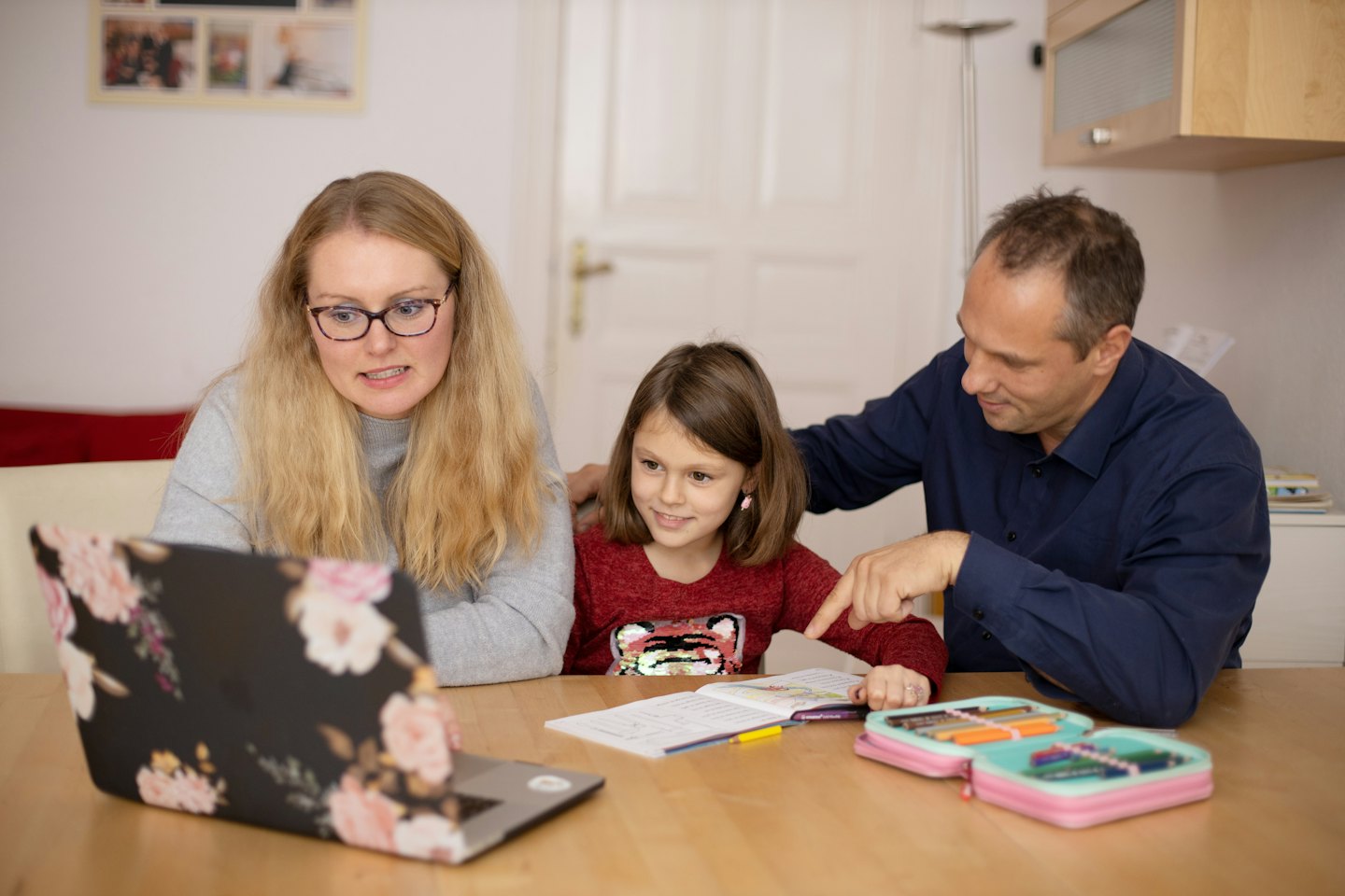 Parents help daughter with schoolwork at a laptop.